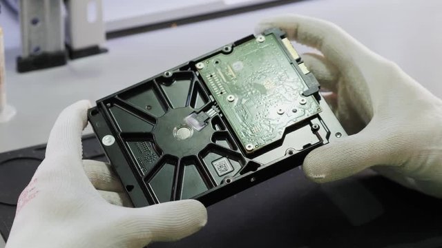 A male repairman wearing white gloves is holding a hard drive from computer or laptop in hands. Performs fault diagnostics and performs urgent repairs recovery of lost data during deletion HDD close