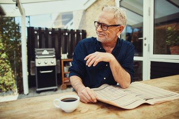 Senior man reading a newspaper outside and drinking coffee