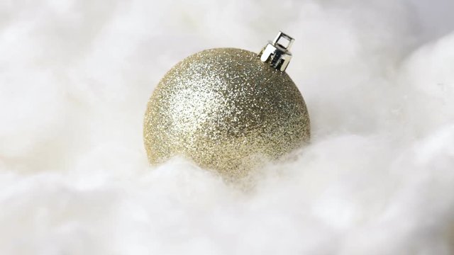 Close up of rotating gold bauble on cotton wool. No sound.