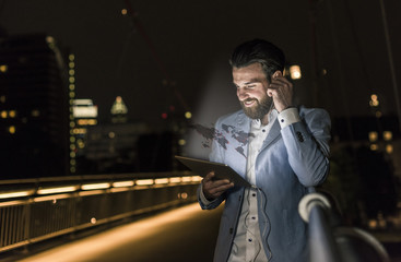 Young man on bridge at night with world map emerging from tablet