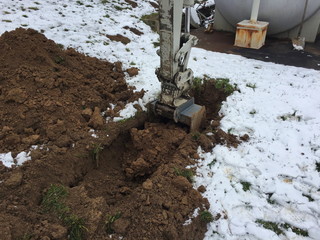 Baggerschaufel gräbt sich in einen Boden, der mit Schnee bedeckt ist