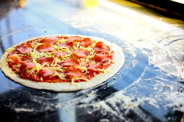 Raw pizza gets ready for baking. Ingredients of yummy pizza have pepperoni, mozzarella cheese, tomato sauce. It looks delicious or yummy food. It’s italian food.  The pizza place near window. sunlight