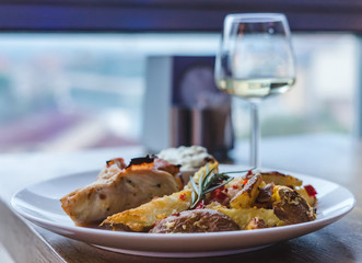 Restaurant meal, meat, potatoes and sauce. Glass of white wine on wooden table