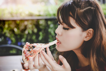 Pizza look so yummy or delicious food. Charming beautiful asian woman is eating pepperoni pizza and sticky mozzarella cheese. Attractive girl is enjoying the taste and loves it. She sit at pizzeria.