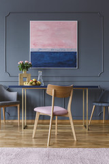 Pink wooden chair at table in dining room interior with painting on grey wall with molding