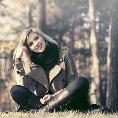 Fototapeta na wymiar Happy young fashion woman in beige coat sitting on grass outdoor