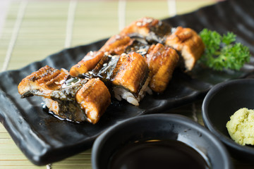 Unagi sushi on black plate along with Japanese sauce and green leaf decoration, Japanese food, close up at sushi..
