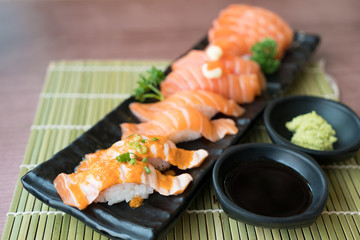 Fototapeta na wymiar Mixed salmon sushi on black plate along with Japanese sauce and green leaf decoration, Japanese food, close up at sushi ..