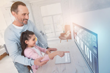 Pointing finger. Emotional young man standing behind his curious daughter and holding her by the elbow while looking at the new device on the wall