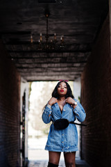 Obraz premium African american girl in jeans dress posed on streets of city. Black stylish model shoot.