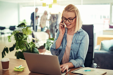 Obraz premium Smiling young businesswoman talking on a cellphone at her desk
