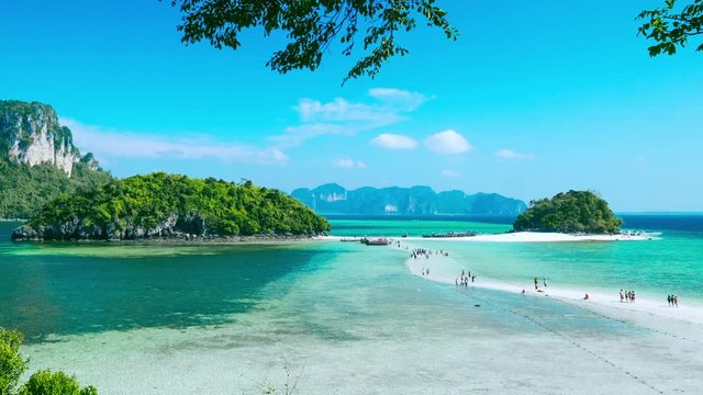 Gorgeous scenery with limestone rock formation, tourists walking along sand spit, moored vessels and tropical azure sea. Boat tour to Koh Tub and Koh Mor islands. Krabi province, Thailand. Time lapse 