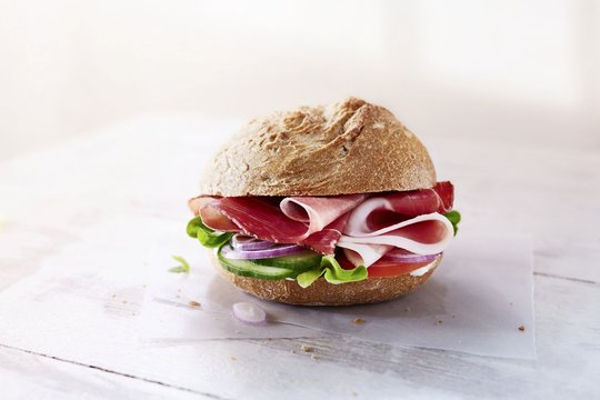 A rye bread role with ham, vegetables and lettuce