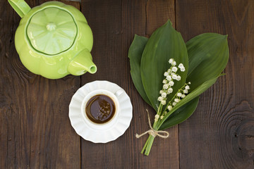 Fresh garden concept: Black coffee, lily of the valley and green kettle on wooden background
