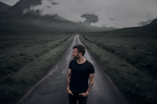 Young man standing on road against cloudy sky
