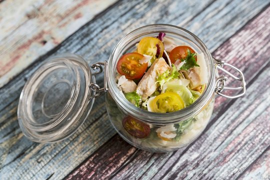 A pasta salad in a glass jar with tomatoes, chicken strips and pecorino