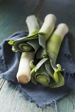 Three whole leeks on a blue cloth and green wooden surface