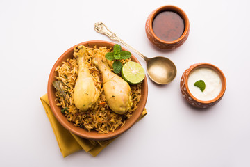 Indian Chicken Biryani served in a terracotta bowl with yogurt over white background. selective focus