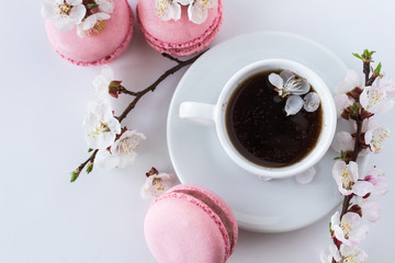 Pink macaroons with a cup of coffee and a branch of white flowers on a white background. French dessert and flowers blooming cherry. Sakura flowers with pink macaroon close up.