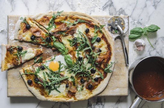 Pizza with tomato sauce, fried egg, rocket, olives and parmesan (top view)