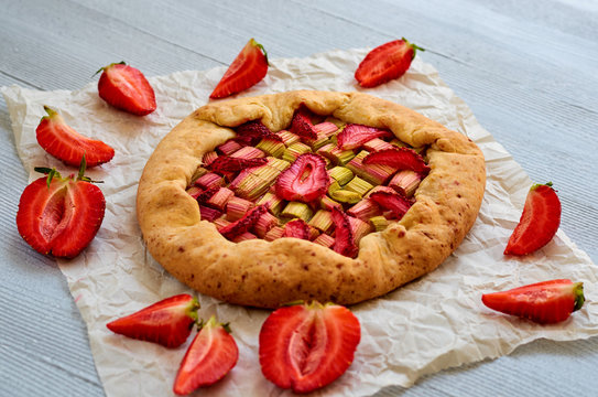 Rhubarb tart with strawberry on the gray concrete background. Vegetarian healthy rhubarb galette decorated with fresh sliced strawberries. Delicious summer dessert. Side view