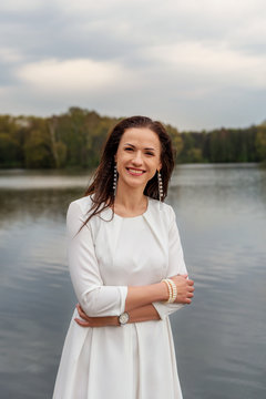 smiling  optimistical confident woman coach standing on waterfront city river lake in white dress