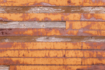 The wooden wall is covered with iron boards. Rusty boards. Texture of rust and wood. Orange rusty background of boards.