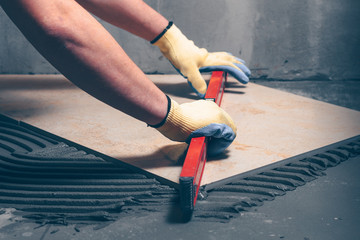 Worker finisher checks the quality of tile works on the floor with the help of a building level,...