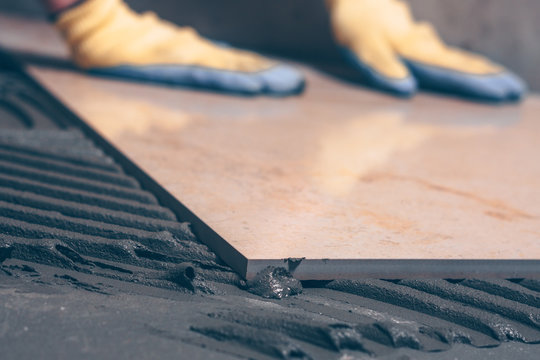 Close-up of a tile stacked on the floor, selective focus, hands of a tiler in the background unfocused