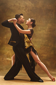 Dance ballroom couple in gold dress dancing on studio background.