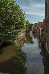 Fototapeta na wymiar Canal with old buildings on the border, leafy tree and blue sky in Bruges. With many canals and old buildings, this graceful town is a World Heritage Site of Unesco. Northwestern Belgium.