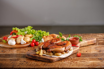 Fried chicken with garnish of baked young potatoes with fresh vegetables. Appetizing still life on a wooden background.