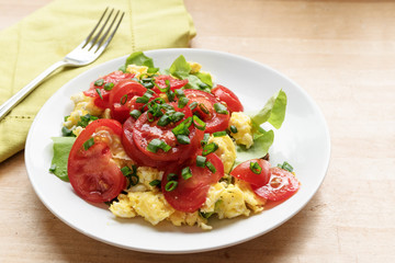 healthy eating, tomatoes on scrambled eggs and green lettuce with chive garnish, white plate on a wooden table