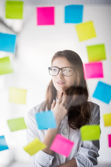 Young beauty business woman thinkin over task stickers on office glass