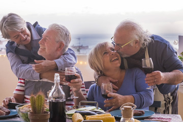 two mature couple stay together with love smiles and kisses during a dinner outdoor on the terrace rooftop with ocean and roofs view. joy and having fun in leisure activity by night and friendship 