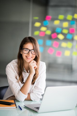 Portrait of a cheerful business woman sitting at the table in office and looking at camera