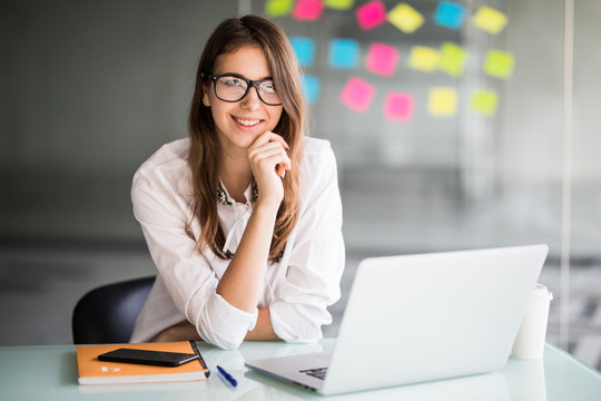 Portrait of a cheerful business woman sitting at the table in office and looking at camera