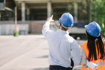 Asian man and woman engineer with the blue safety helmet meeting at the construction site with...