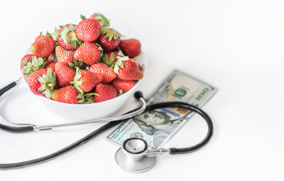 Fresh summer strawberries on a white background with medical stethoscope and monye banknote one hundred dollars. The concept of healthy food and prices increase