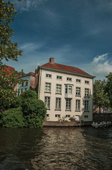 Greenery and brick buildings on the canal's edge in a sunny day at Bruges. With many canals and old buildings, this graceful town is a World Heritage Site of Unesco. Northwestern Belgium.