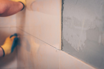 The working tiler wipes the tile on the wall with a damp sponge, removes the glue residues from the...