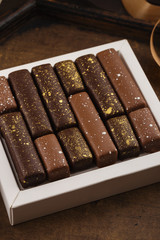 Handmade bonbons with gold splashes in box on wooden background