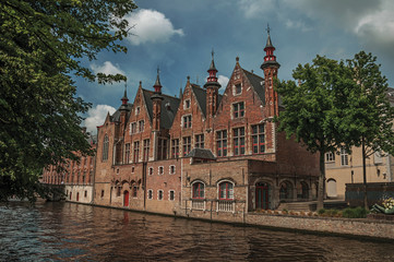 Wooded gardens and brick buildings on the canal's edge in a sunny day at Bruges. With many canals and old buildings, this graceful town is a World Heritage Site of Unesco. Northwestern Belgium.