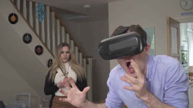 Woman upset with VR cheating man headset AI. Handheld shot of millennial man wearing VR headset clearly doing something naughty, girlfriend finds him and gets upset, leaving