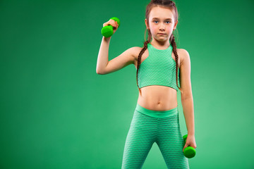 Kid girl doing fitness exercises with dumbbells on green background