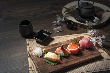 Many delicious sushi on wooden tray with tea set.
