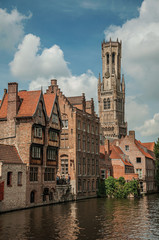 Old brick buildings and belfry on the canal's edge in a sunny day at Bruges. With many canals and old buildings, this graceful town is a World Heritage Site of Unesco. Northwestern Belgium.