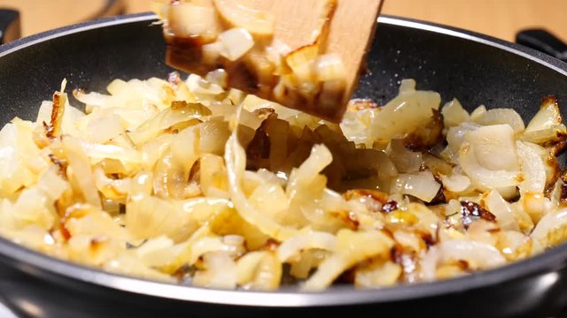 Chopped onions fried  in hot frying pan, hand mixing with wooden spoon spatula. Vegetable preparing, meals with vegetables. Slow motion.
