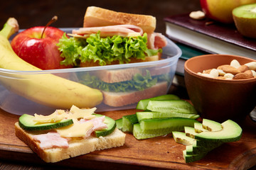 School or picnic lunch box with sandwich and various colorful vegetables and fruits on wooden background, close up.