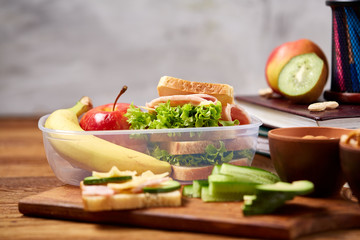 School or picnic lunch box with sandwich and various colorful vegetables and fruits on wooden background, close up.